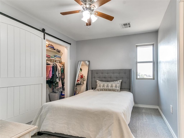 carpeted bedroom with a barn door, ceiling fan, a closet, and a spacious closet