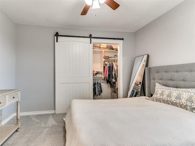 bedroom featuring ceiling fan, a barn door, a walk in closet, light carpet, and a closet