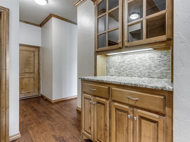 kitchen with decorative backsplash, light stone counters, dark hardwood / wood-style floors, and ornamental molding