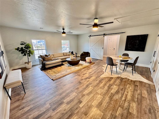 living room featuring ceiling fan, a barn door, a textured ceiling, and wood-type flooring