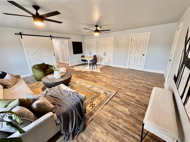 living room featuring wood-type flooring, ceiling fan, and a barn door