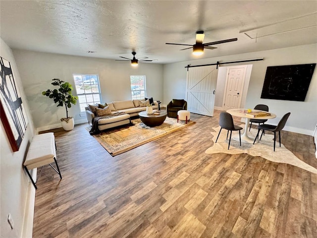 living room featuring a textured ceiling, hardwood / wood-style floors, ceiling fan, and a barn door