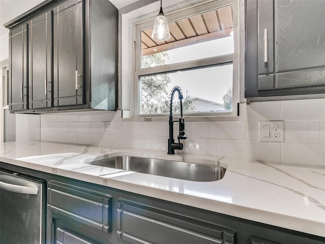 kitchen featuring light stone countertops, dishwasher, hanging light fixtures, backsplash, and sink