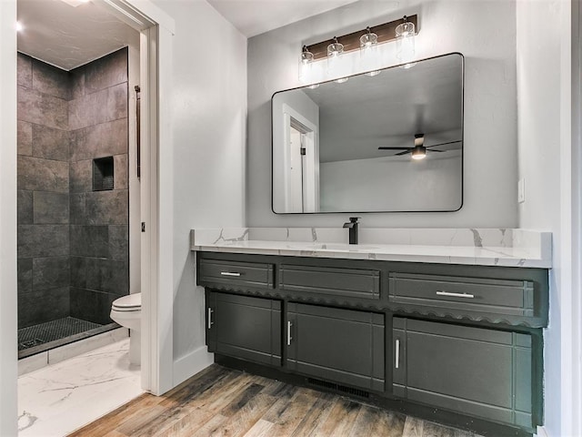 bathroom with ceiling fan, tiled shower, vanity, and toilet