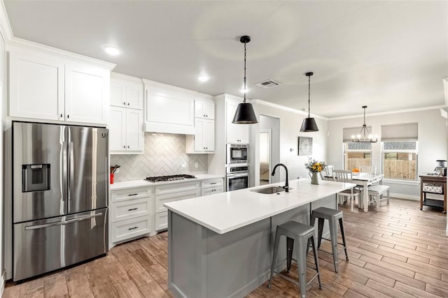 kitchen with a center island with sink, appliances with stainless steel finishes, ornamental molding, white cabinets, and sink