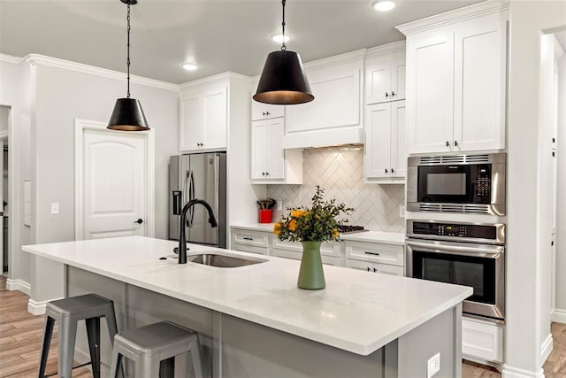 kitchen with white cabinets, a center island with sink, stainless steel appliances, sink, and decorative light fixtures