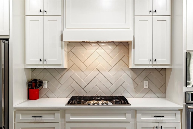 kitchen featuring stainless steel gas cooktop, ventilation hood, white cabinetry, fridge, and backsplash