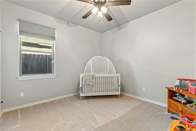 carpeted bedroom featuring ceiling fan and a crib