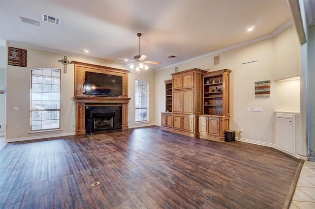 unfurnished living room with dark wood-type flooring, plenty of natural light, ornamental molding, and ceiling fan