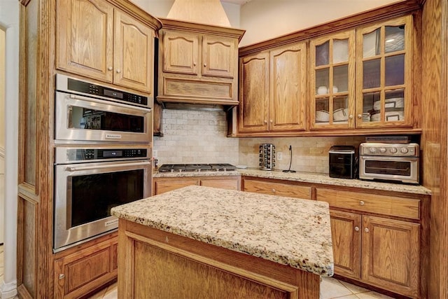 kitchen with light tile patterned flooring, appliances with stainless steel finishes, light stone countertops, and backsplash