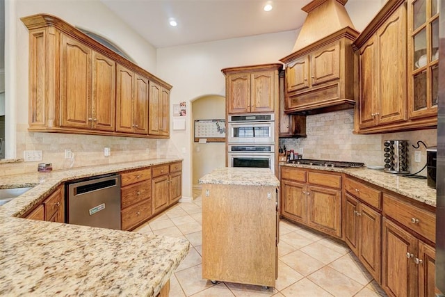 kitchen featuring a kitchen island, backsplash, light tile patterned floors, stainless steel appliances, and light stone countertops