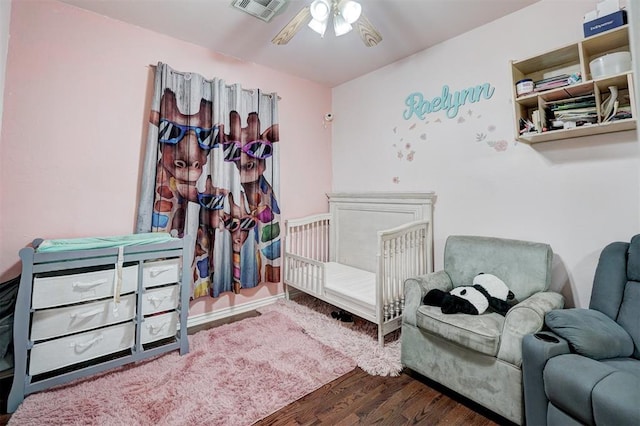 bedroom with dark hardwood / wood-style floors, a nursery area, and ceiling fan