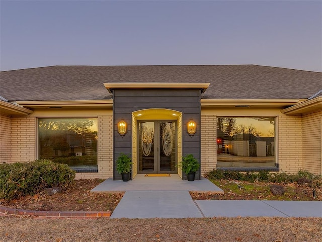 view of exterior entry featuring brick siding and roof with shingles