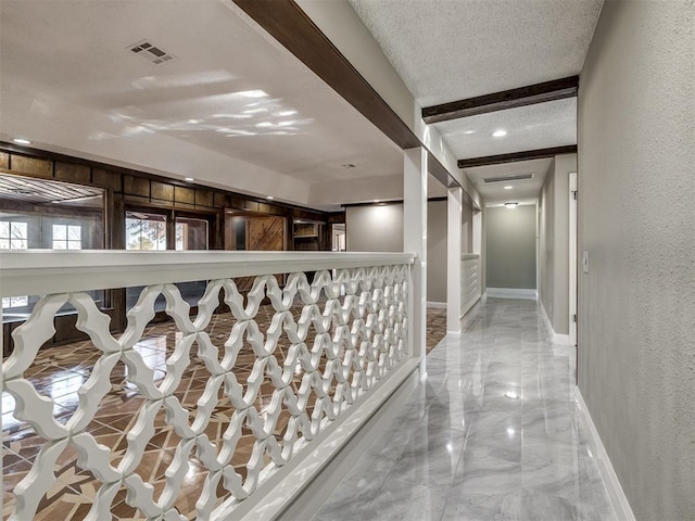 hall with visible vents, marble finish floor, a textured ceiling, and a textured wall