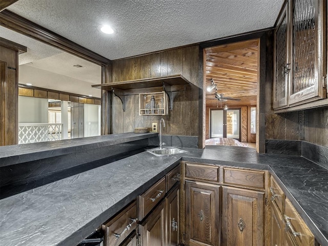 kitchen featuring open shelves, a sink, wood walls, a textured ceiling, and dark countertops