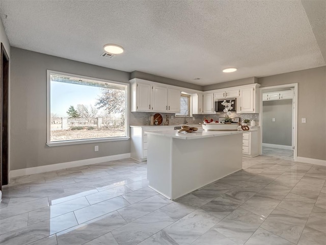 kitchen with stainless steel microwave, visible vents, light countertops, white cabinets, and marble finish floor