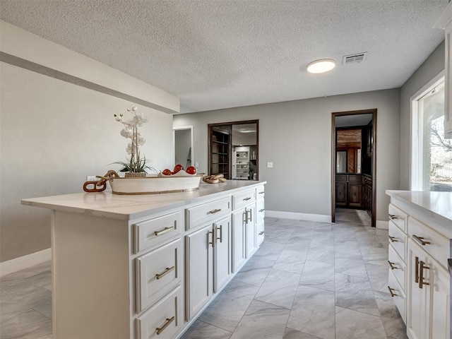 kitchen with white cabinets, a center island, light stone countertops, and a textured ceiling