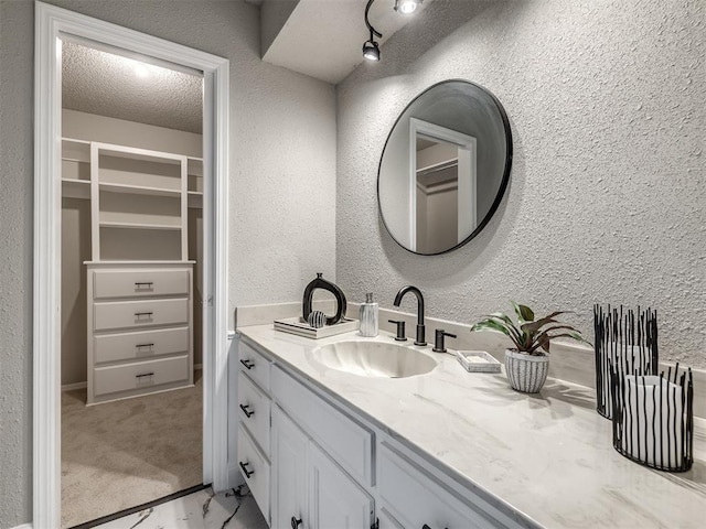 bathroom featuring a walk in closet, vanity, a textured wall, and a textured ceiling