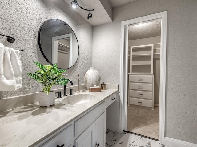 bathroom featuring marble finish floor, a textured ceiling, a spacious closet, vanity, and a textured wall