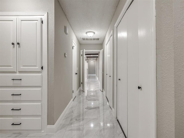 corridor featuring baseboards, visible vents, a textured ceiling, a textured wall, and marble finish floor