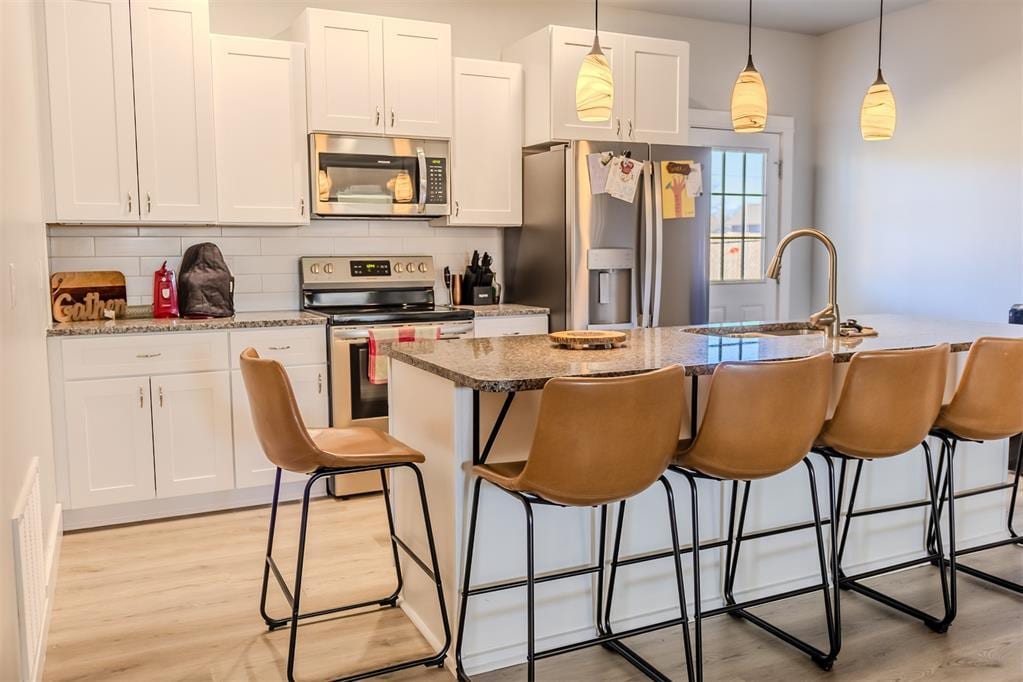 kitchen featuring appliances with stainless steel finishes, white cabinetry, hanging light fixtures, a kitchen island with sink, and light stone counters