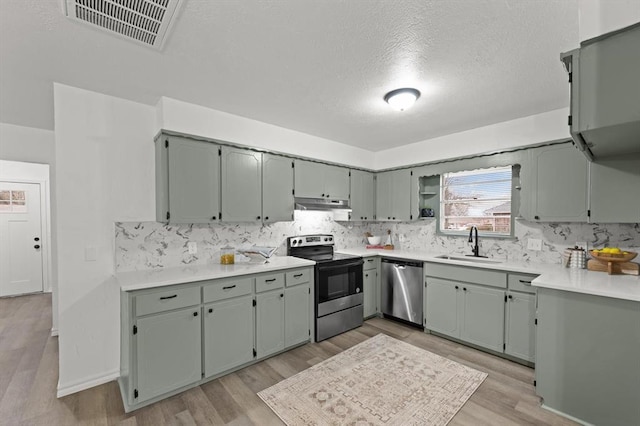 kitchen with light wood-type flooring, appliances with stainless steel finishes, sink, and a textured ceiling