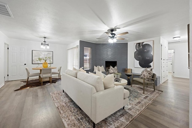 living room with a large fireplace, ceiling fan with notable chandelier, and hardwood / wood-style floors