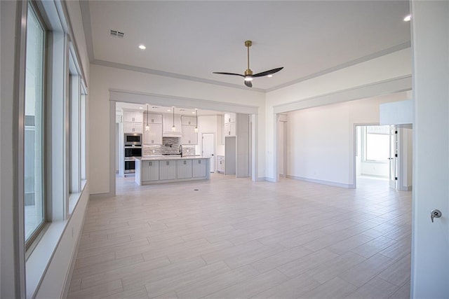 unfurnished living room with ceiling fan and crown molding