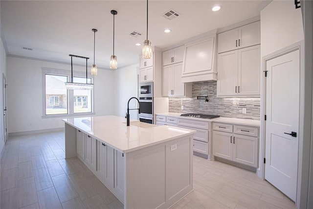 kitchen with custom range hood, sink, white cabinets, and an island with sink