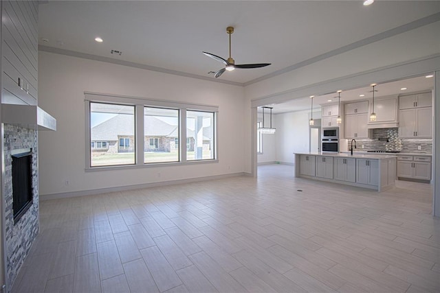 unfurnished living room featuring a stone fireplace, ceiling fan, light wood-type flooring, crown molding, and sink