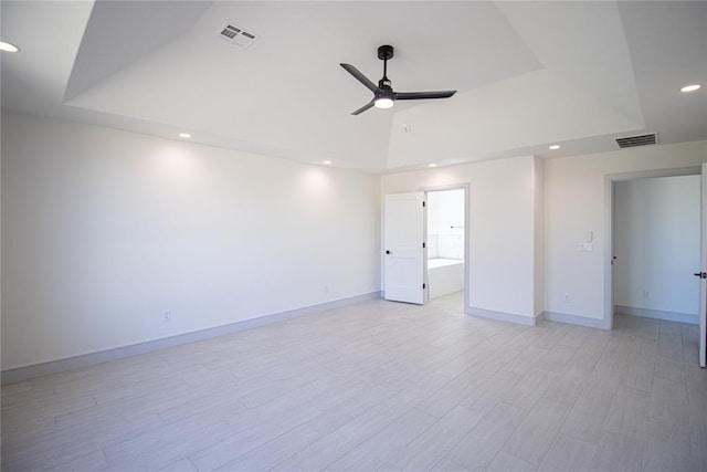 empty room with a raised ceiling, ceiling fan, and light hardwood / wood-style floors