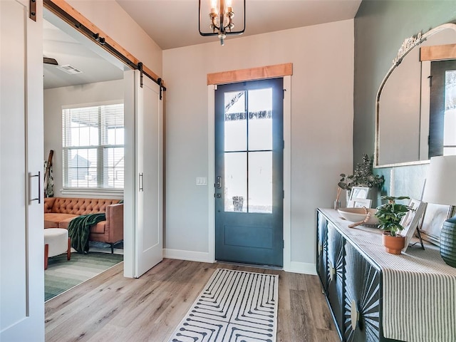 foyer with a barn door, light hardwood / wood-style floors, and a chandelier