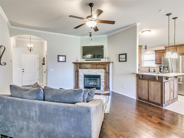 living room featuring a stone fireplace, dark hardwood / wood-style flooring, ceiling fan with notable chandelier, and ornamental molding