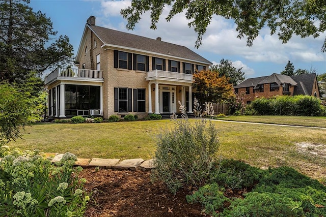 colonial home featuring a sunroom, a balcony, and a front yard