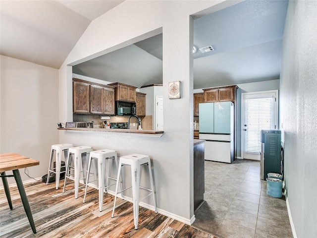 kitchen with lofted ceiling, backsplash, white refrigerator, a kitchen bar, and kitchen peninsula