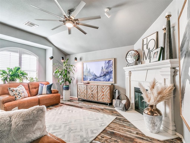 living room featuring ceiling fan, vaulted ceiling, a tile fireplace, and light hardwood / wood-style flooring