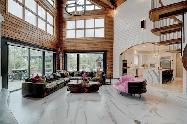 living room featuring a chandelier, a high ceiling, wooden walls, and beamed ceiling