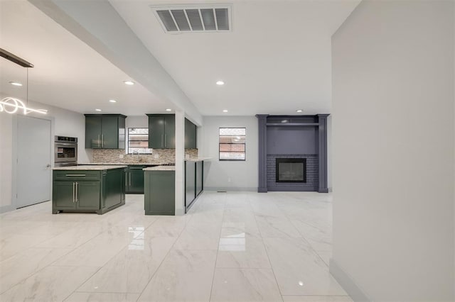 kitchen with pendant lighting, stainless steel oven, a brick fireplace, green cabinetry, and tasteful backsplash