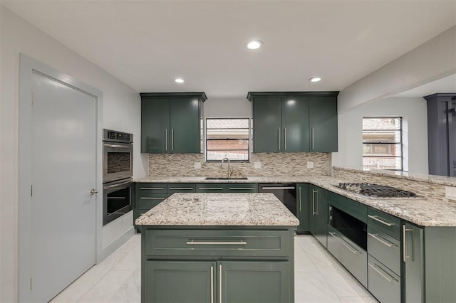 kitchen with decorative backsplash, light stone counters, stainless steel appliances, sink, and green cabinets