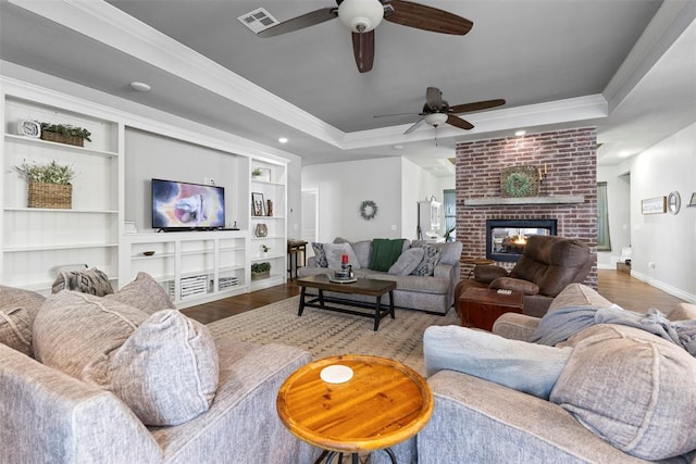 living room with a fireplace, hardwood / wood-style floors, a raised ceiling, and crown molding