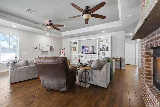 living room with a raised ceiling, ceiling fan, a fireplace, and dark hardwood / wood-style floors