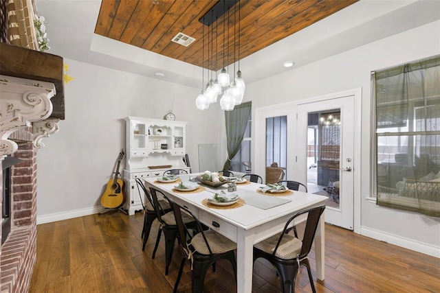 dining area featuring a brick fireplace, a tray ceiling, dark wood-type flooring, an inviting chandelier, and wooden ceiling