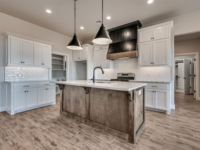 kitchen featuring sink, decorative light fixtures, white cabinets, stainless steel gas stove, and an island with sink