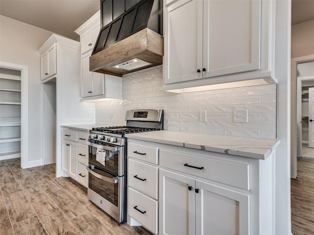 kitchen featuring white cabinets, stainless steel gas stove, light wood-type flooring, light stone counters, and custom range hood