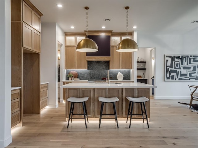 kitchen featuring tasteful backsplash, an island with sink, hanging light fixtures, and light wood-type flooring