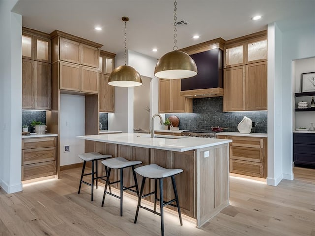 kitchen with a center island with sink, light wood-type flooring, custom range hood, and sink