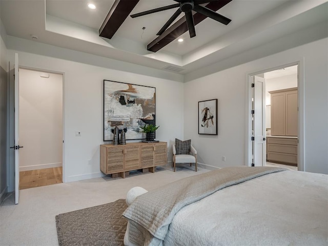 bedroom with a raised ceiling, ceiling fan, ensuite bathroom, and light carpet