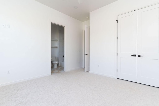 unfurnished bedroom featuring light colored carpet, ensuite bath, and a closet