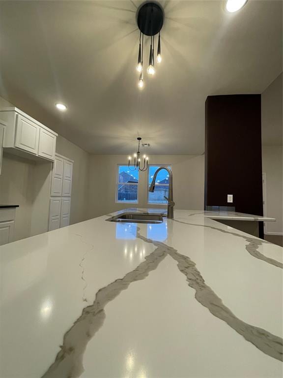 kitchen with pendant lighting, an inviting chandelier, sink, light stone counters, and white cabinetry