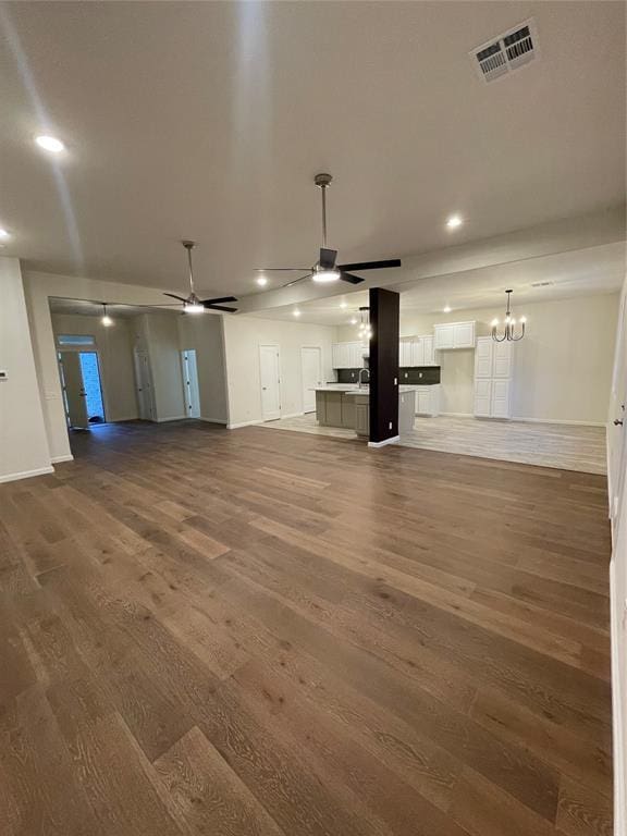 unfurnished living room with ceiling fan with notable chandelier and dark hardwood / wood-style floors